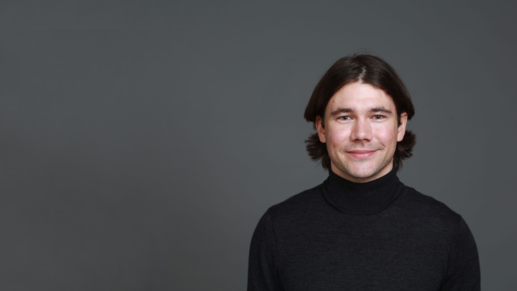 Profile image of Julian Bushmass showing him wearing a black turtleneck against a dark grey background