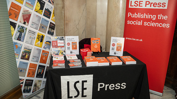 LSE Press promotional stand at an event with branded banners, table cloth, leaflets and books on display