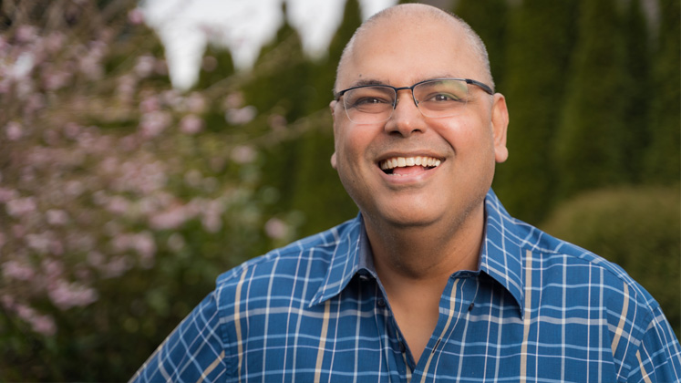 Alex sangha smiles standing beside a tree in bloom