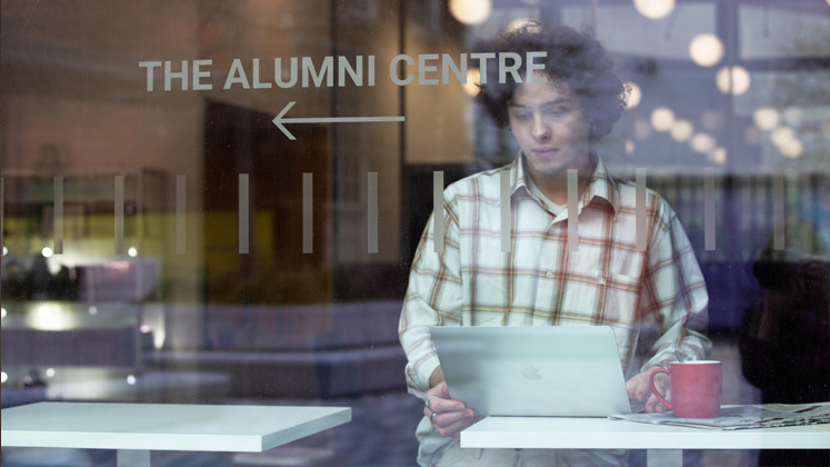 A man works on a laptop by the window of LSE's Alumni Centre