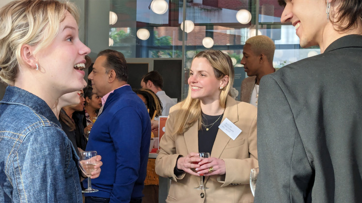 Two alumni chat as people mingle in the background at the launch of LSE's LGBTQ+ Alumni Network