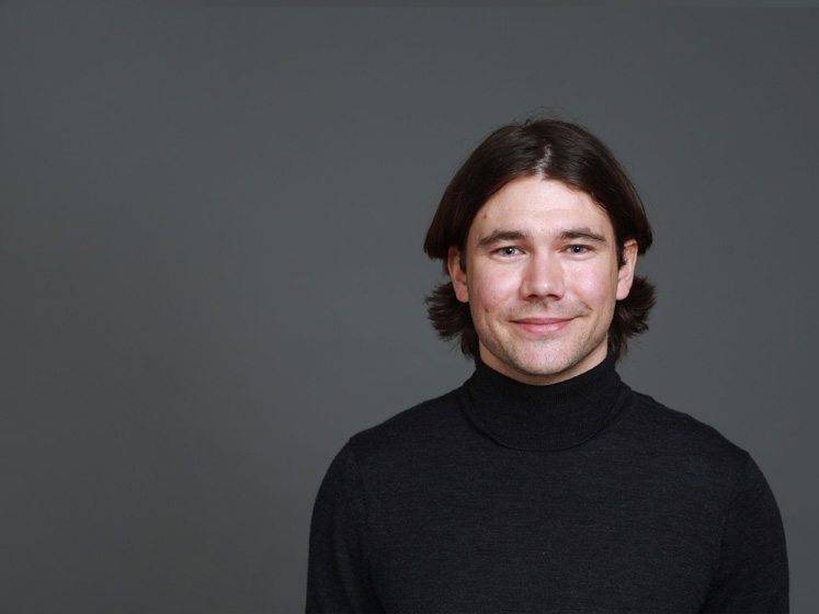 Profile image of Julian Bushmass showing him wearing a black turtleneck against a dark grey background