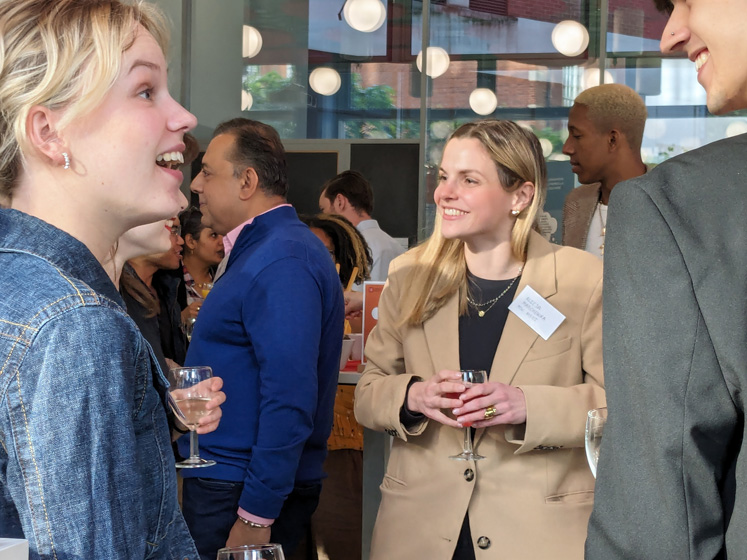 Two people chat in the Alumni Centre as people mingle in the background