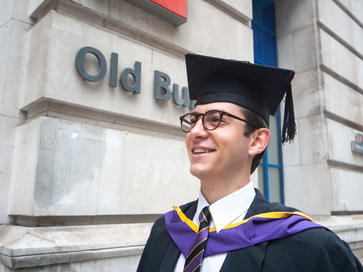 Fabio wears his graduation gap and gown outside LSE's Old Building