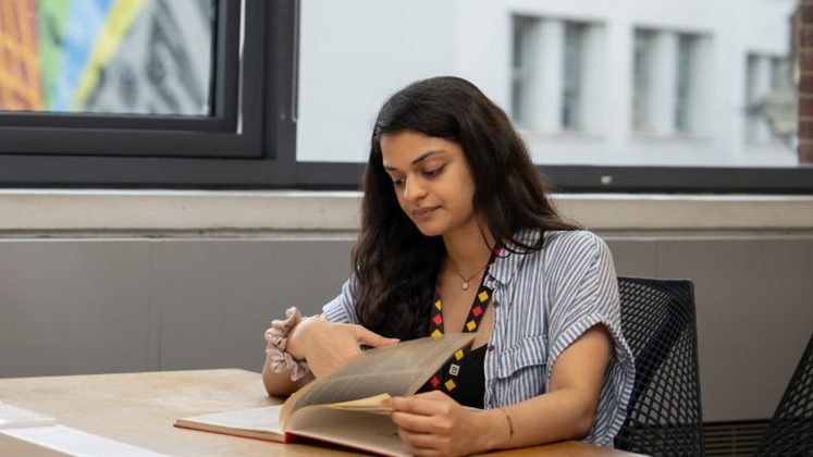 A person sat studying in LSE Library. Outside there is a piece of artwork in view