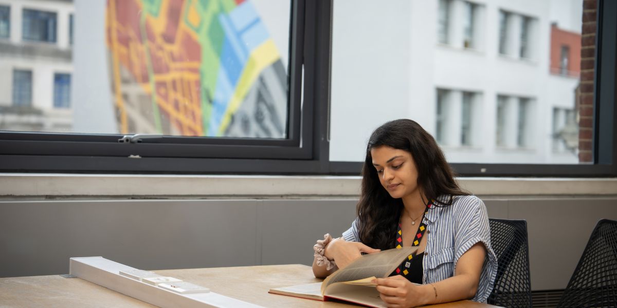 A person sat studying in LSE Library. Outside there is a piece of artwork in view