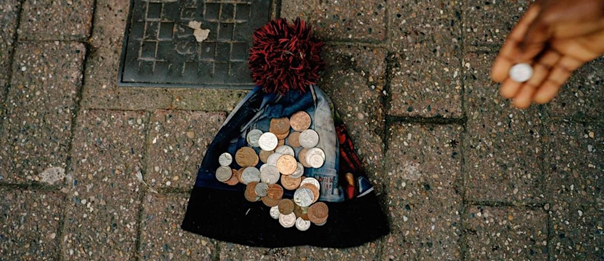 Money on top of a bobble hat laid on a pavement