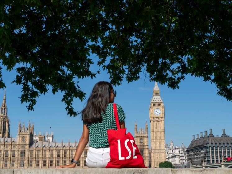 student sitting facing Big Ben with LSE tote bag