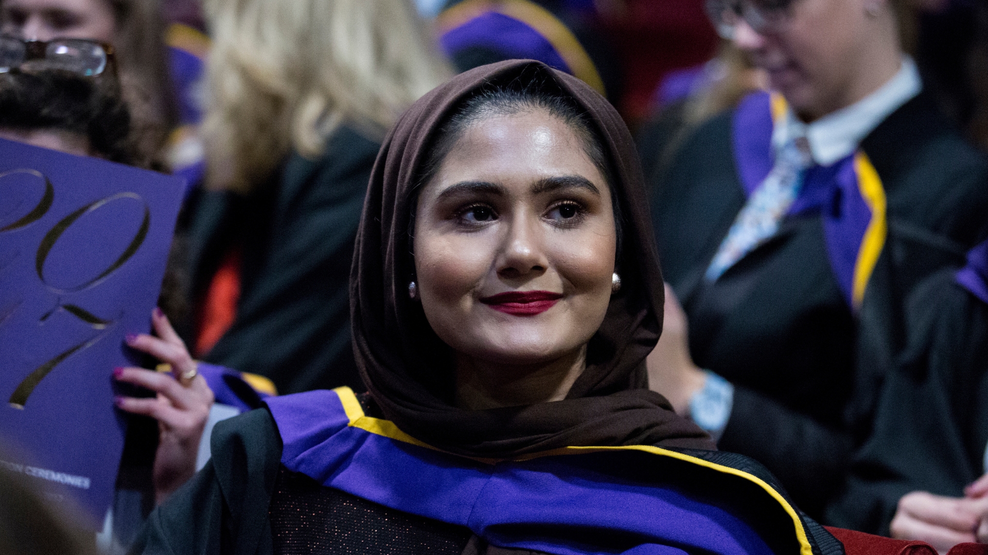 Female student in graduation gown with a headscarf smiling to camera