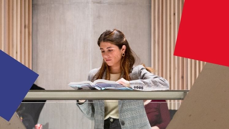 Female student reading from a box on a landing in the Marshall Building.