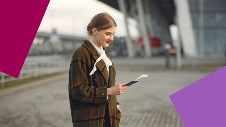 Female student at an airport looking down at their passport and boarding pass.