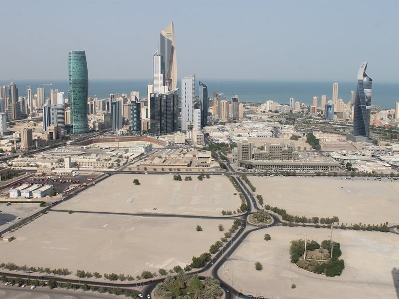 An aerial shot of Kuwait City, with stretches of empty space in the foreground and skyscrapers in the background.