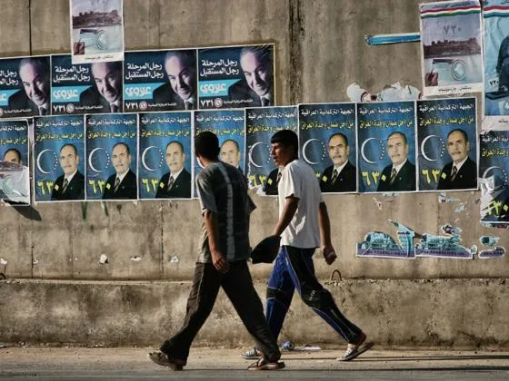 Two young men walk past a concrete wall with posters attached to it