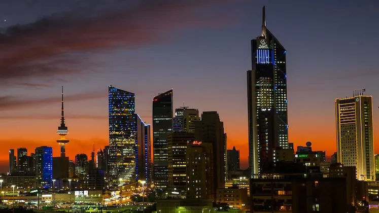 Kuwait City skyline at dusk, skyscrapers lit up with a red-blue background