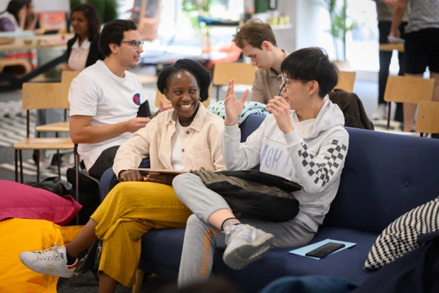 Two students in conversation sat on sofa in GenDen