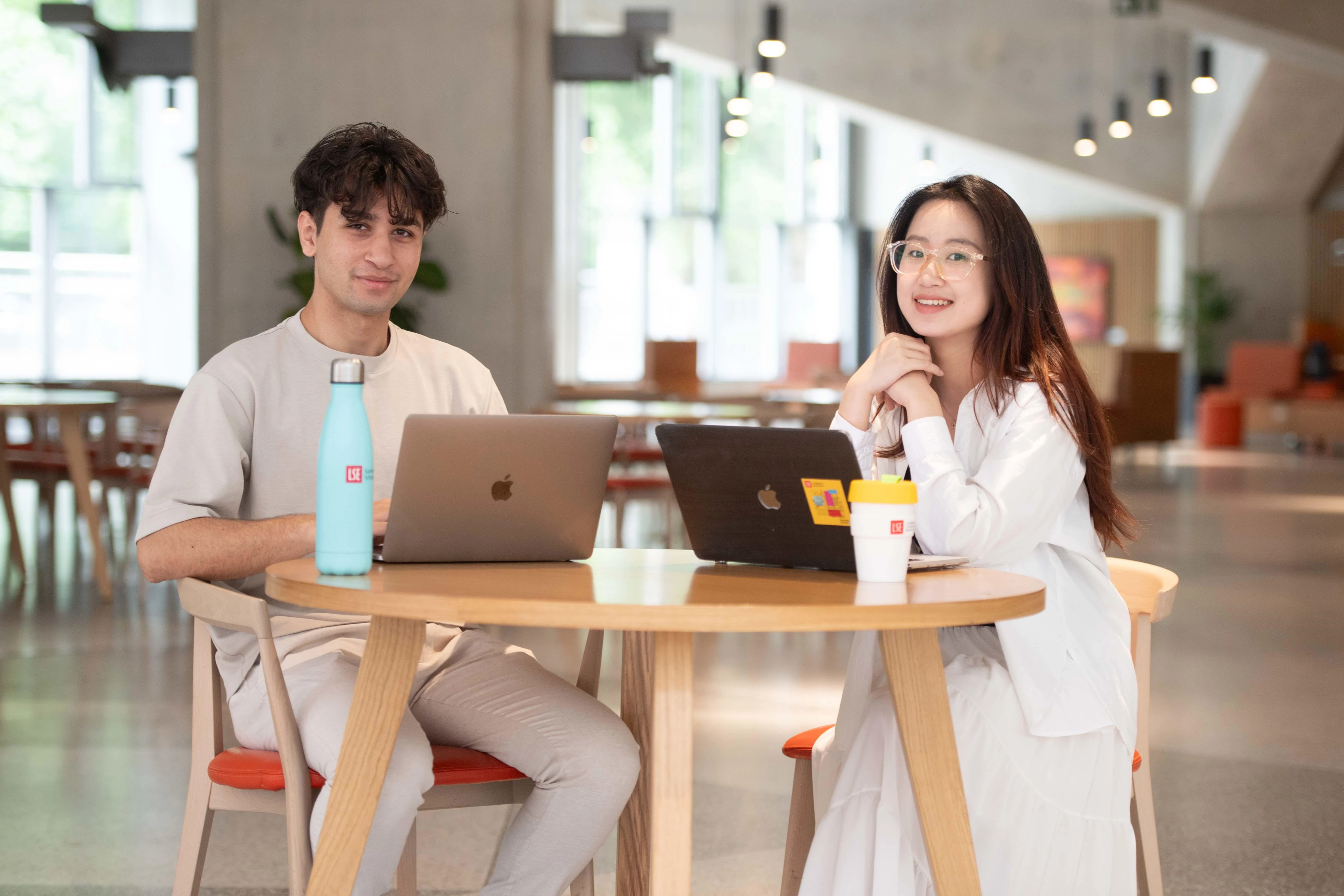 Two students sat at table in Marshall Building with laptops